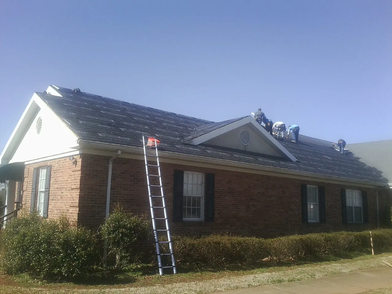 Crew tearing shingles off a brick ranch roof with a ladder set — Emergency Roof Repair work by our crew in Rushville